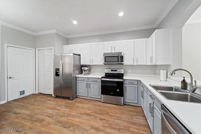 kitchen with gray cabinetry, appliances with stainless steel finishes, ornamental molding, a sink, and light wood-type flooring