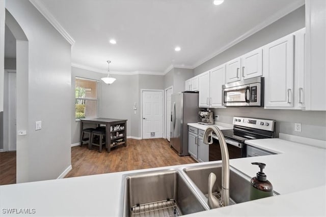 kitchen with ornamental molding, appliances with stainless steel finishes, pendant lighting, white cabinets, and hardwood / wood-style flooring