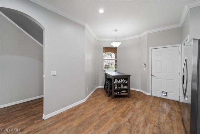 dining room featuring arched walkways, ornamental molding, wood finished floors, and baseboards