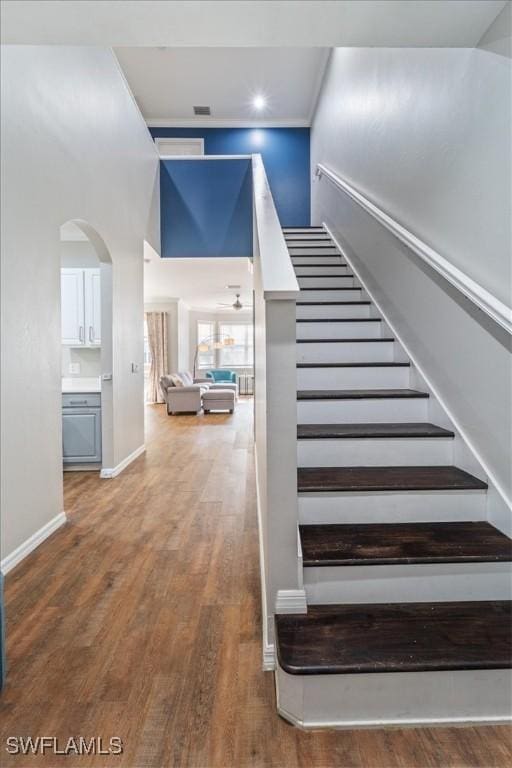 staircase featuring arched walkways, a towering ceiling, baseboards, and wood finished floors