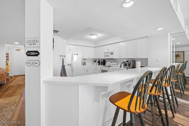 kitchen with kitchen peninsula, a kitchen breakfast bar, white appliances, dark wood-type flooring, and white cabinets