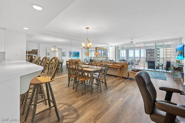 dining area with hardwood / wood-style flooring, ceiling fan with notable chandelier, and a wall of windows