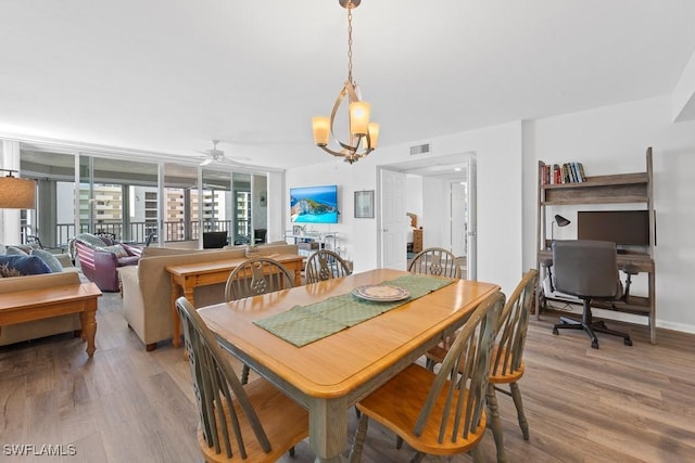 dining space with ceiling fan with notable chandelier and light hardwood / wood-style flooring