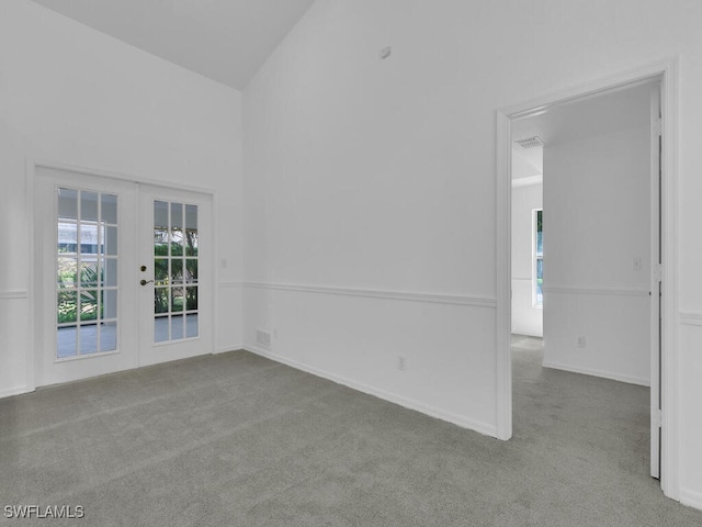 carpeted spare room featuring french doors and high vaulted ceiling