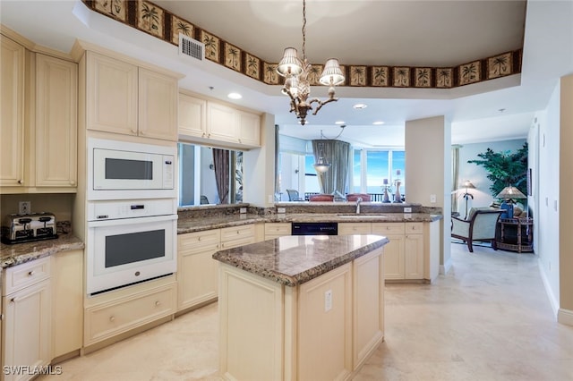 kitchen with kitchen peninsula, white appliances, decorative light fixtures, an inviting chandelier, and cream cabinetry