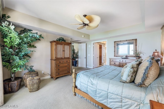 carpeted bedroom featuring a tray ceiling, connected bathroom, and ceiling fan