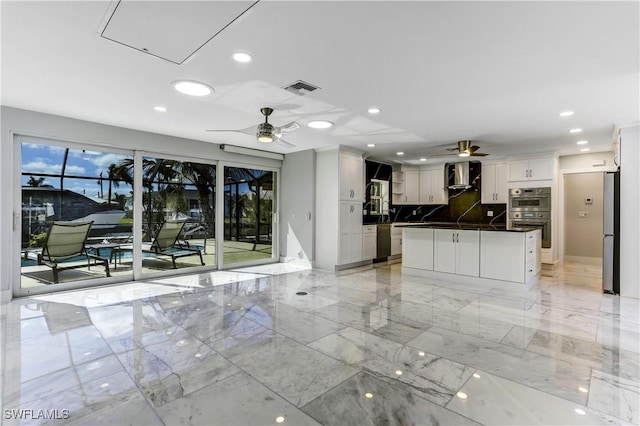 kitchen with white cabinetry, a center island, ceiling fan, wall chimney range hood, and appliances with stainless steel finishes