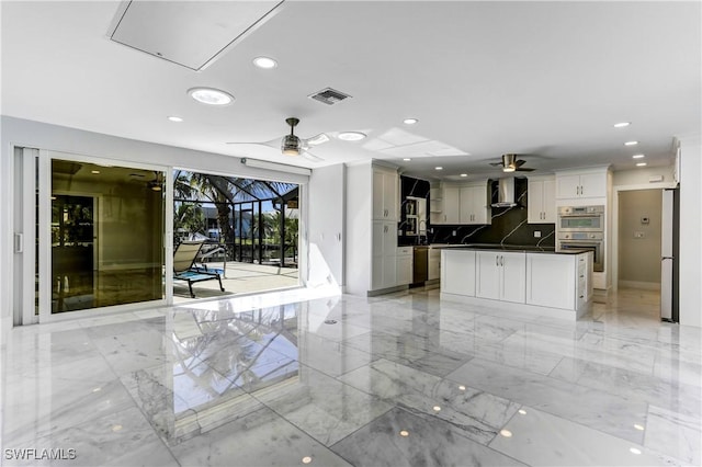 kitchen with appliances with stainless steel finishes, white cabinetry, wall chimney exhaust hood, and ceiling fan