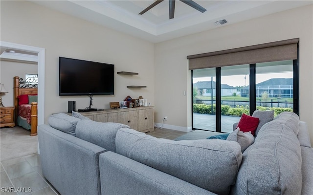 living room with light tile patterned floors, a tray ceiling, and ceiling fan