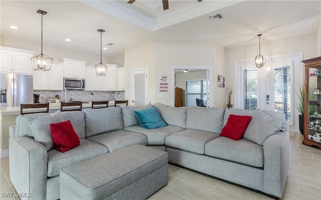 tiled living room with a raised ceiling, ceiling fan, and crown molding