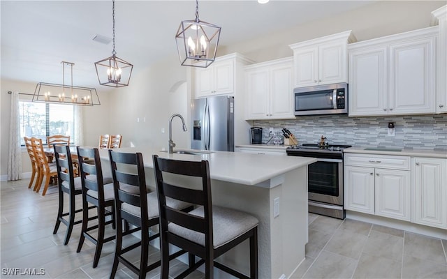 kitchen with white cabinets, decorative backsplash, an island with sink, and appliances with stainless steel finishes