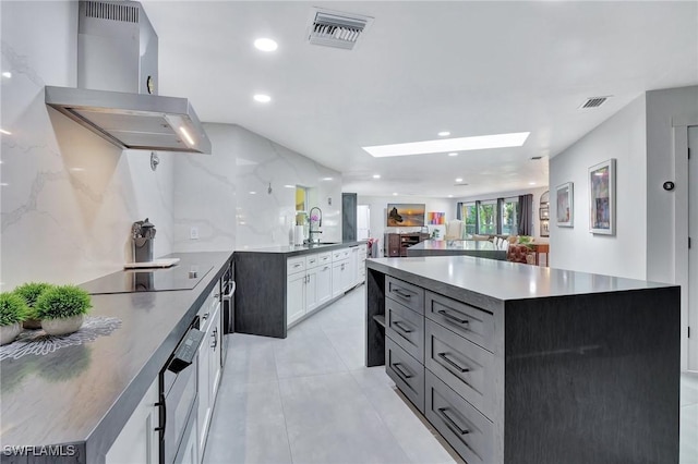 kitchen with a skylight, a kitchen island, extractor fan, black electric cooktop, and white cabinets