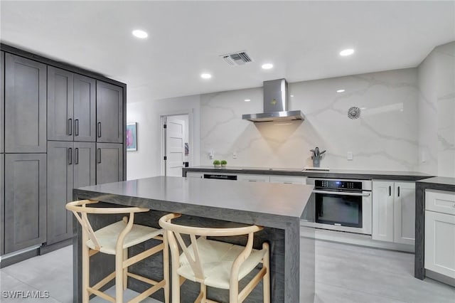 kitchen featuring wall chimney range hood, tasteful backsplash, oven, a breakfast bar, and a kitchen island