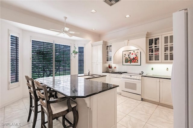 kitchen featuring a kitchen breakfast bar, tasteful backsplash, ceiling fan, white stove, and a kitchen island