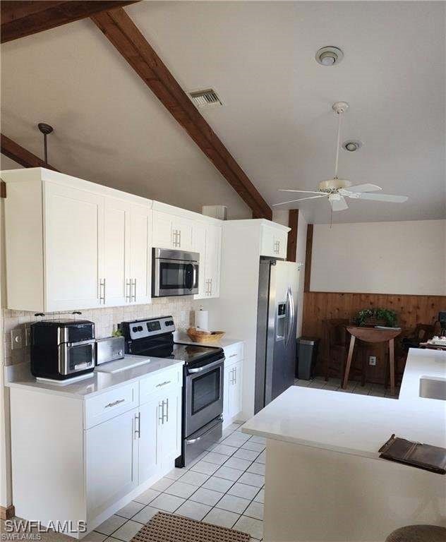 kitchen featuring appliances with stainless steel finishes, ceiling fan, light tile patterned floors, beam ceiling, and white cabinetry