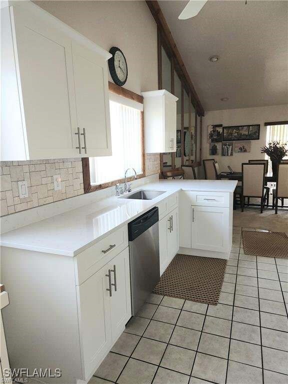 15188 Sam Snead Ln, North Fort Myers, FL 33917 - kitchen featuring stainless steel dishwasher, a sink, light tile patterned floors, white cabinets, and light countertops