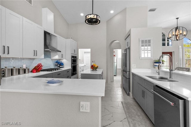 kitchen with white cabinets, backsplash, hanging light fixtures, stainless steel appliances, and wall chimney exhaust hood