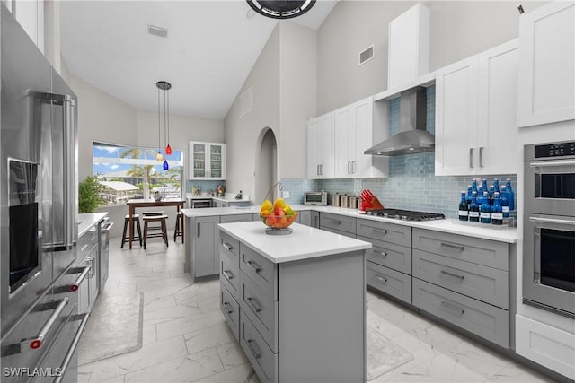 kitchen with wall chimney range hood, white cabinetry, stainless steel appliances, high vaulted ceiling, and tasteful backsplash