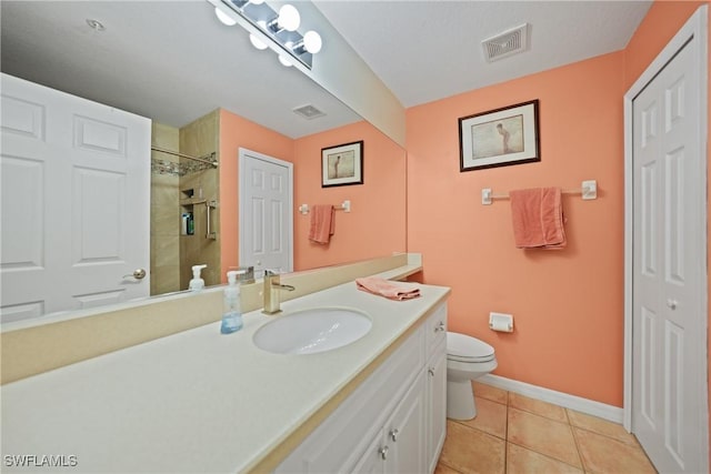 bathroom with tile patterned flooring, vanity, tiled shower, and toilet