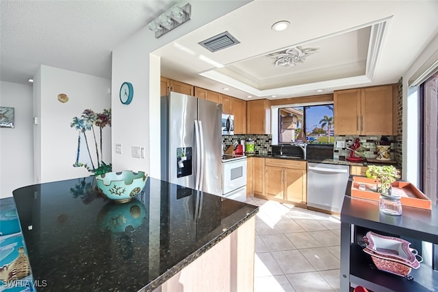 kitchen with appliances with stainless steel finishes, tasteful backsplash, a raised ceiling, light tile patterned floors, and dark stone countertops