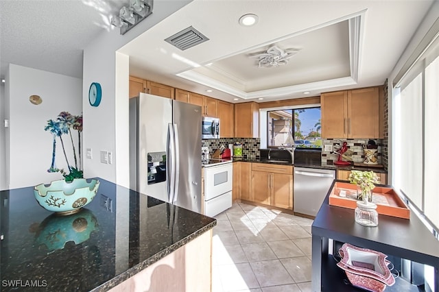 kitchen with stainless steel appliances, a raised ceiling, dark stone counters, decorative backsplash, and light tile patterned floors