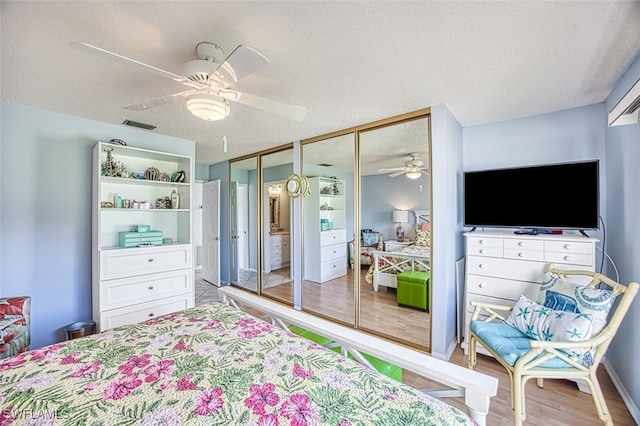 bedroom featuring wood-type flooring, a textured ceiling, ceiling fan, and multiple closets