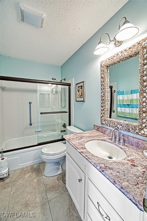 full bathroom with vanity, a textured ceiling, toilet, and enclosed tub / shower combo