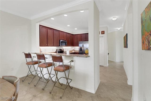 kitchen featuring kitchen peninsula, appliances with stainless steel finishes, light stone counters, ornamental molding, and a breakfast bar area