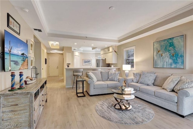 living room with light wood-type flooring, ornamental molding, and a tray ceiling