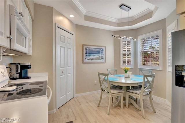 dining area featuring a raised ceiling, light hardwood / wood-style floors, a notable chandelier, and ornamental molding