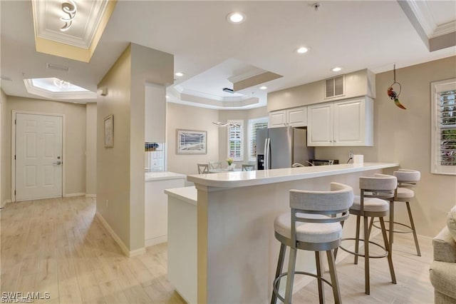 kitchen featuring white cabinets, stainless steel fridge with ice dispenser, a breakfast bar area, and a tray ceiling