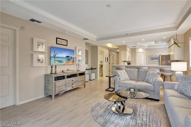 living room with light hardwood / wood-style floors, a raised ceiling, and ornamental molding