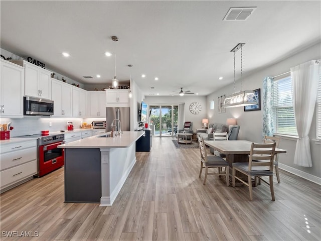 kitchen featuring a kitchen island with sink, white cabinets, hanging light fixtures, and appliances with stainless steel finishes