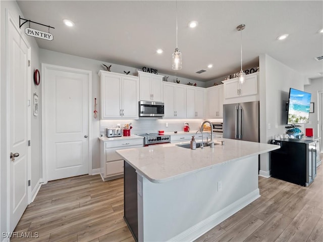 kitchen with appliances with stainless steel finishes, sink, pendant lighting, a center island with sink, and white cabinets