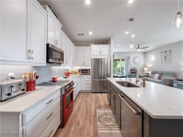 kitchen with pendant lighting, high end appliances, white cabinets, sink, and ceiling fan