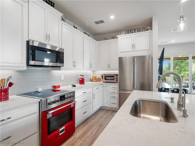 kitchen with sink, hanging light fixtures, light hardwood / wood-style floors, white cabinetry, and stainless steel appliances