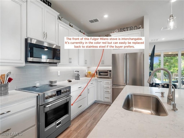 kitchen with sink, light stone countertops, light wood-type flooring, premium appliances, and white cabinetry