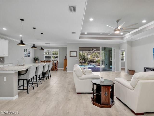 living room with ornamental molding, a raised ceiling, ceiling fan, and sink