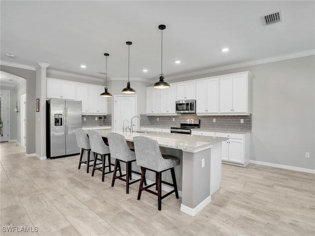 kitchen featuring stainless steel appliances, white cabinetry, light stone counters, an island with sink, and pendant lighting