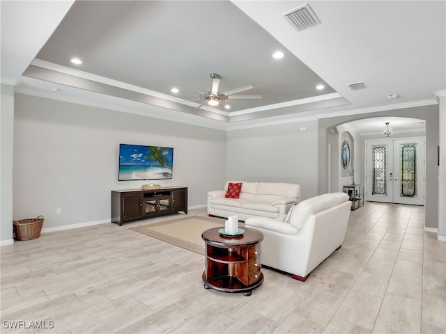 living room featuring ceiling fan with notable chandelier, ornamental molding, french doors, and a tray ceiling