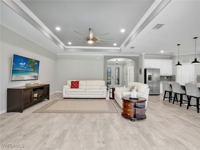 living room featuring ornamental molding, ceiling fan, light wood-type flooring, and a raised ceiling