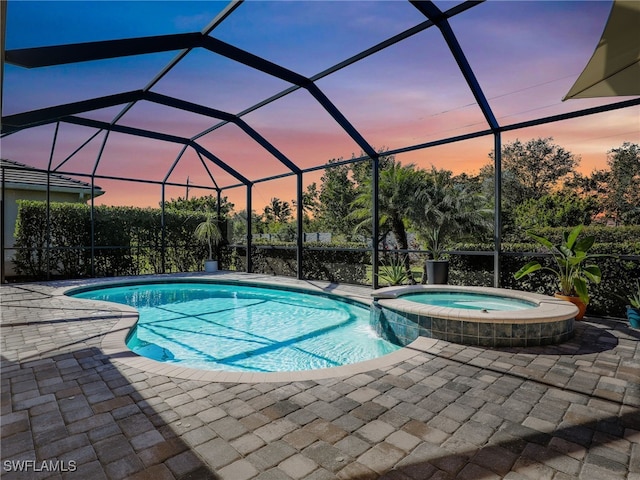 pool at dusk with a patio, glass enclosure, and an in ground hot tub