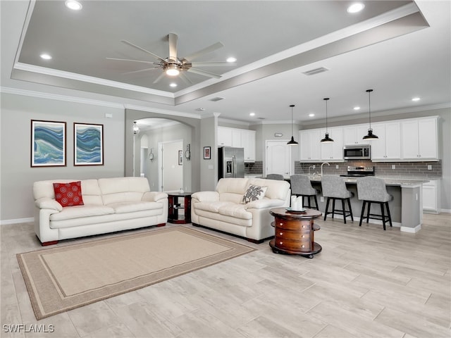 living room featuring ceiling fan, a raised ceiling, and crown molding