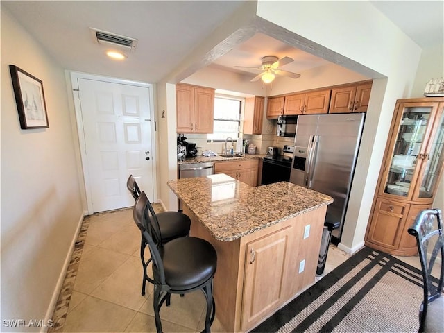 kitchen with light stone countertops, sink, a center island, light tile patterned floors, and appliances with stainless steel finishes