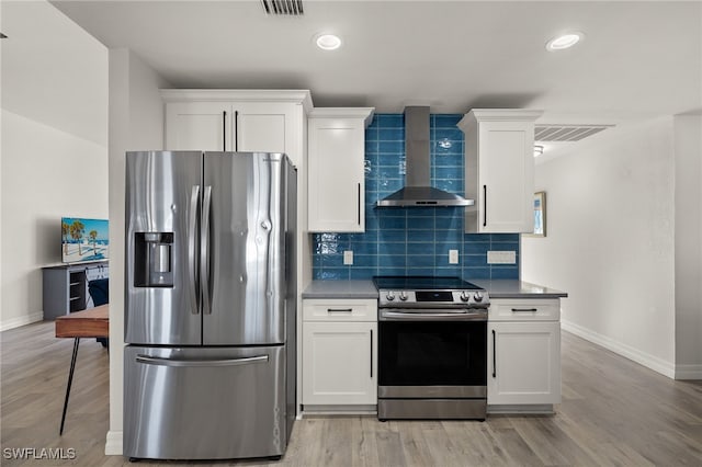 kitchen featuring appliances with stainless steel finishes, white cabinetry, and wall chimney range hood