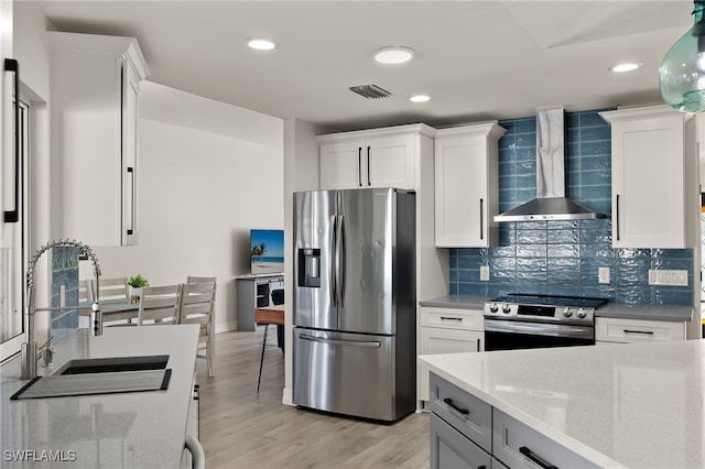 kitchen featuring appliances with stainless steel finishes, white cabinetry, wall chimney exhaust hood, and sink