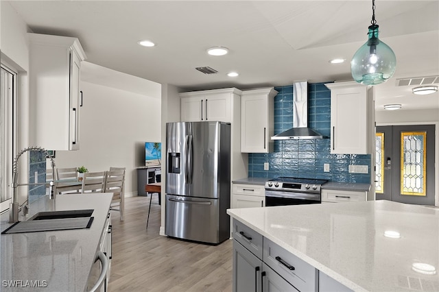 kitchen featuring white cabinets, wall chimney range hood, sink, light stone countertops, and stainless steel appliances