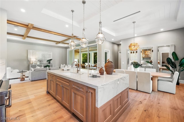 kitchen with pendant lighting, light wood-type flooring, sink, and a large island with sink