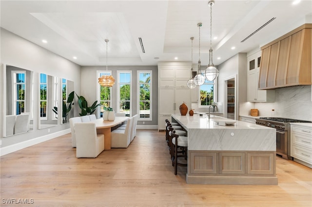 kitchen with a large island, hanging light fixtures, high end stainless steel range oven, light hardwood / wood-style flooring, and a tray ceiling