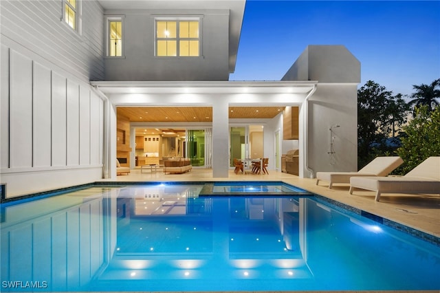 back of house at dusk with an outdoor pool, a patio, and an in ground hot tub